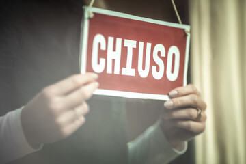 Close up of a females hands holding door sign 'closed'' in Italian