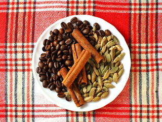 Coffee, cardamom, cinnamon on a white plate. Checkered towel.