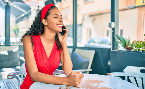 Young african american girl talking on the smartphone sitting on the table at coffee shop terrace.