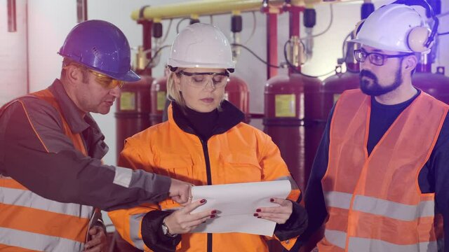 Woman engineer with skilled workers in hardhats and uniform read technical papers checking industrial complex before start
