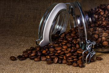 Coffee beans pouring out of a glass jar onto a hessian background