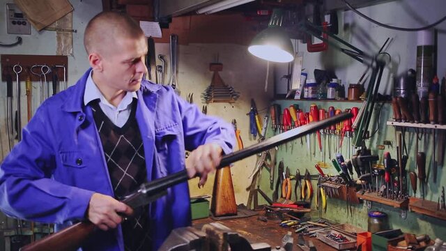 Qualified gunsmith performing checkout of horizontal double rifle before preventive maintenance in weapons workshop