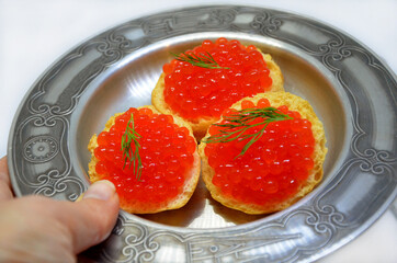 seafood croutons with red caviar on a plate in hand closeup