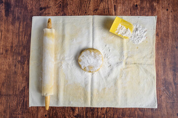 Preparation for baking, ball of sugar cookie dough on a pastry cloth and covered wooden rolling pin on a wood table
