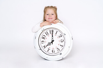 The girl is sitting on the floor in front of a large white clock. Isolated over white background.