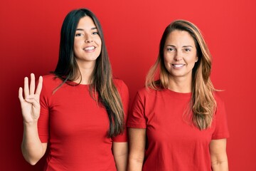 Hispanic family of mother and daughter wearing casual clothes over red background showing and pointing up with fingers number four while smiling confident and happy.