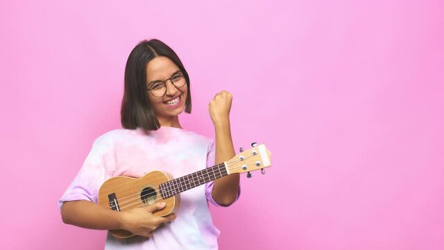 Young latin woman playing ukelele raising fist after a victory, winner concept