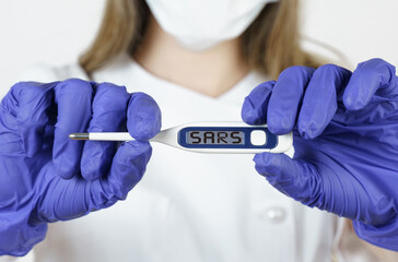 The doctor holds a thermometer in his hands, on the electronic screen of which it is written - SARS