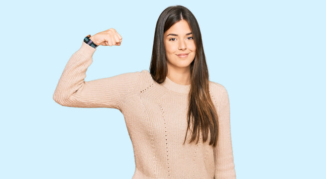 Young brunette woman wearing casual winter sweater strong person showing arm muscle, confident and proud of power