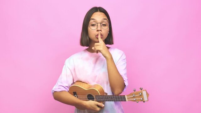 Young latin woman playing ukelele keeping a secret or asking for silence