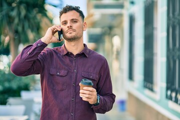 Young hispanic man with serioys expression talking on the smartphone and drinking coffee at the...