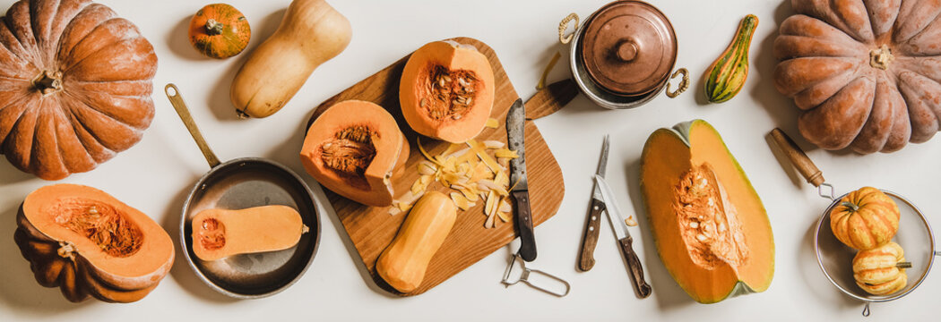 Fall or winter vegan cooking. Flat-lay of cleaning and cooking pumpkin on wooden board over white table with different pumpkins and kitchenware for cooking, top view. Vegan, vegetarian food © sonyakamoz