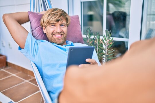 Middle age handsome man at the terrace of his house relaxing lying on a hammock with touchpad device