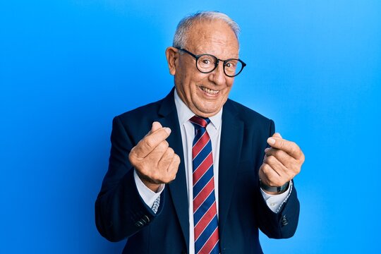 Senior caucasian man wearing business suit and tie doing money gesture with hands, asking for salary payment, millionaire business