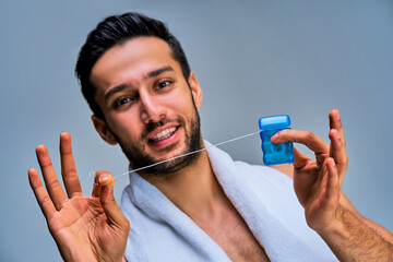 Closeup guy with smile with black hair with a beard pulls dental floss from the packaging. Dental concept