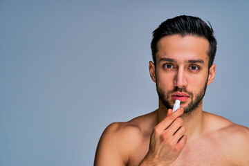 Guy with smile with black hair moisturize paints lips looking at camera. Cosmetics concept © IC Production