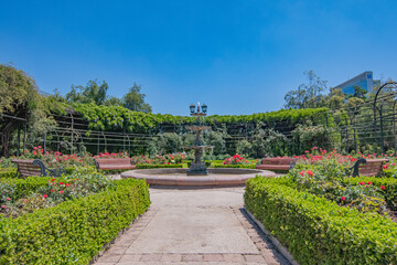 Fototapeta premium Fuente de agua con asientos, árboles y flores.