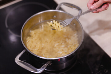 Pasta on a fork over a pot of boiling water and pasta. The process of cooking pasta at home.
