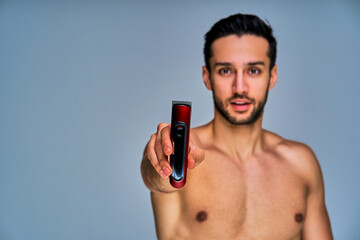Positive guy with black hair with a beard shows electric shaver in hand. Beauty concept