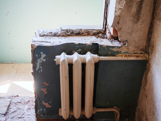 Old white battery on a dilapidated wall in an apartment