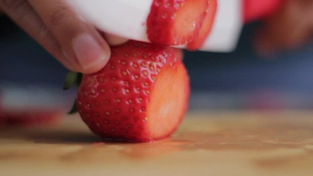 Jugoso corte de fresas en la tabla de una cocina con un cuchillo blanco de cer&aacute;mica 