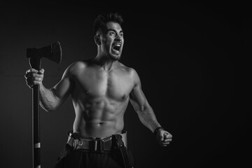 young, handsome, adult, muscular firefighter in uniform holding an ax of fire equipment in his...