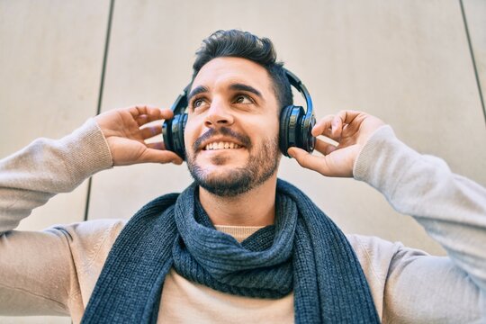 Young hispanic man smiling happy listening to music using headphones at the city.