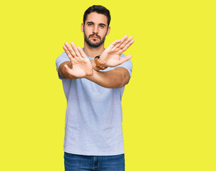 Young hispanic man wearing casual clothes rejection expression crossing arms and palms doing...
