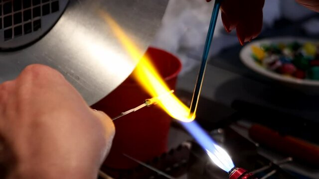 The artist heats the glass with a gas burner. The process of making glass jewelry. Master's hands close-up.
