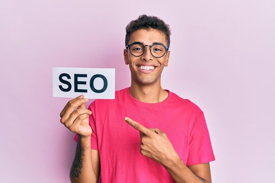 Young handsome african american man holding seo message paper smiling happy pointing with hand and finger