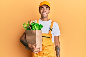 Young handsome african american man wearing courier uniform with groceries from supermarket looking...