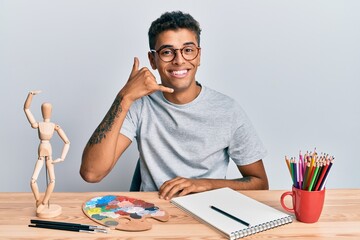 Young handsome african american man painter sitting palette and art manikin smiling doing phone...