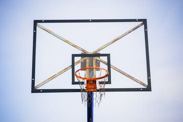 Basketball hoop with transparent board and chains instead of net against the light blue clear sky during the afternoon with a slight dark vignette on the side taken from a lower front angle