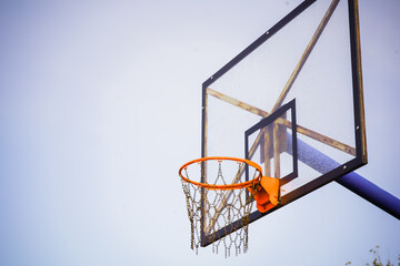 Basketball hoop with transparent board and chains instead of net against the light blue clear sky during the afternoon with a slight dark vignette on the side taken from a lower right angle
