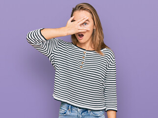 Beautiful blonde woman wearing casual clothes peeking in shock covering face and eyes with hand, looking through fingers with embarrassed expression.