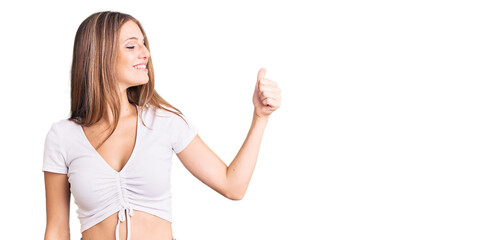 Young beautiful blonde woman wearing casual white tshirt looking proud, smiling doing thumbs up gesture to the side