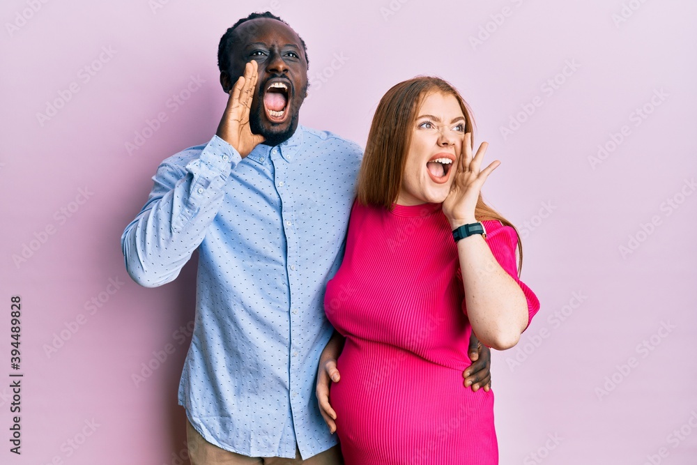 Poster Young interracial couple expecting a baby, touching pregnant belly shouting and screaming loud to side with hand on mouth. communication concept.