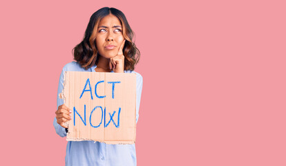 Young beautiful mixed race woman holding act now banner serious face thinking about question with...