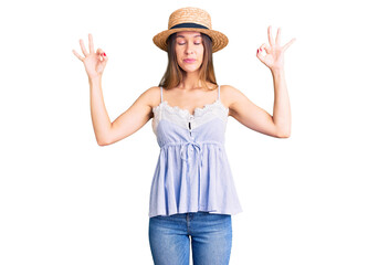 Obraz na płótnie Canvas Beautiful brunette young woman wearing summer hat relax and smiling with eyes closed doing meditation gesture with fingers. yoga concept.