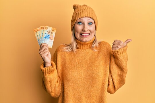 Middle age caucasian woman holding swiss franc banknotes pointing thumb up to the side smiling happy with open mouth