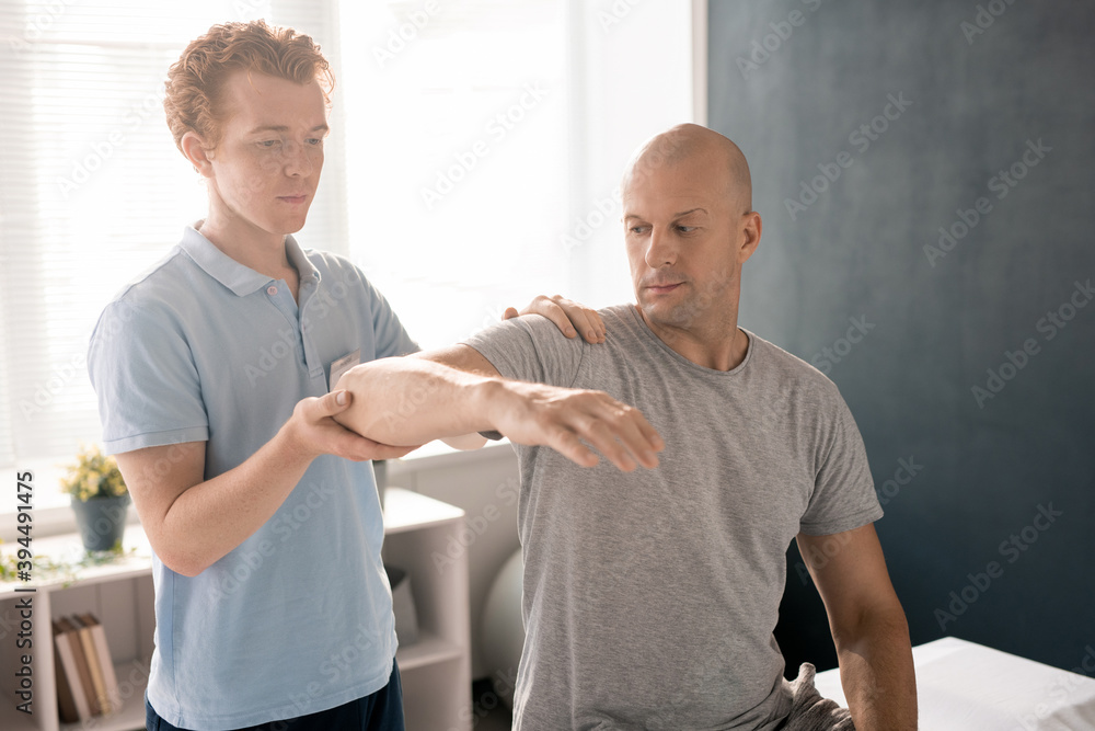 Poster physiotherapist supporting patient arm in elbow while consulting and helping him