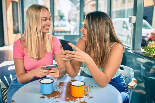 Two beautiful and young girl friends together at cafeteria using smartphone
