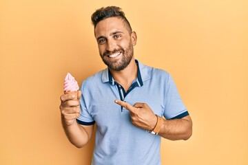 Handsome man with beard eating ice cream cone smiling happy pointing with hand and finger