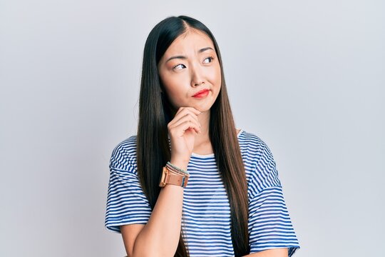 Young chinese woman wearing casual striped t-shirt thinking concentrated about doubt with finger on chin and looking up wondering