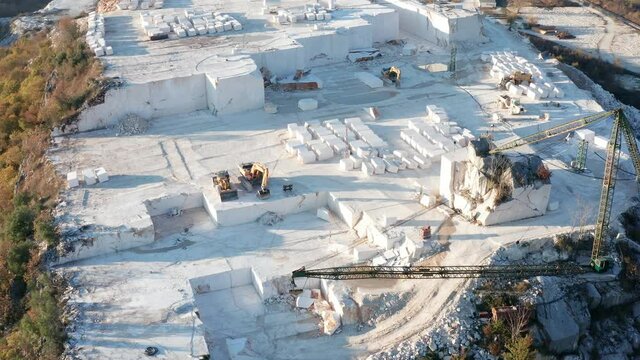 White marble quarry - construction rocks mining in an open-pit mine. Cut stone block and heavy machinery. Aerial drone footage.