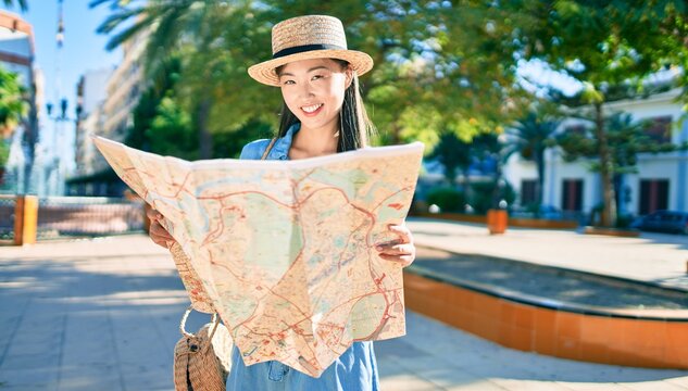 Young chinese tourist woman smiling happy holding city map at the park.