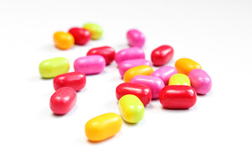 Small pill drops scattered on white surface. Pile of colorful bean shaped candies