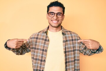 Young handsome hispanic man wearing casual clothes and glasses looking confident with smile on...