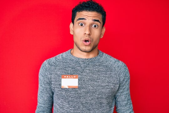 Young handsome hispanic man wearing hello my name is sticker identification scared and amazed with open mouth for surprise, disbelief face