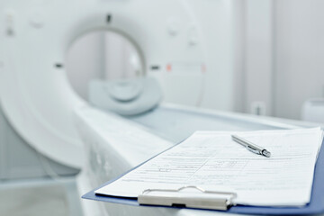Clipboard with medical document and pen on couchette against medical equipment